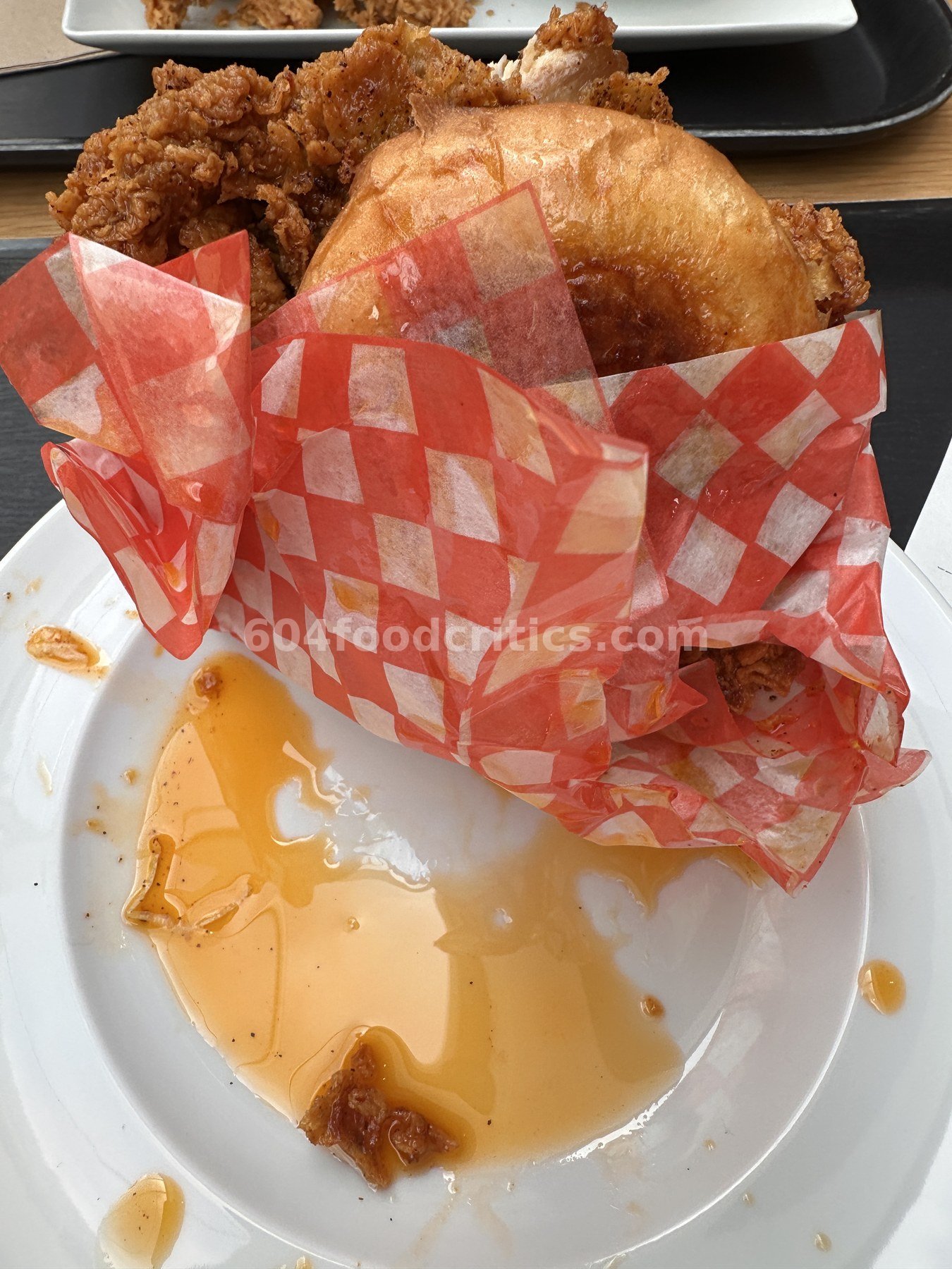 Orange chili oil pooled on a white plate beside the DownLow OG Sando in red-check paper