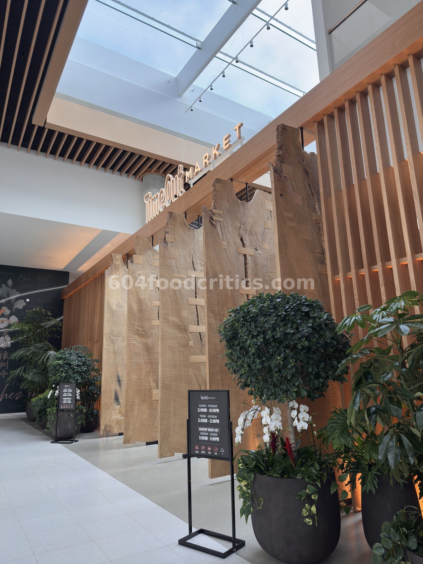 Time Out Market Vancouver entrance at Oakridge Park with skylight, raw-edge wood slabs and plants