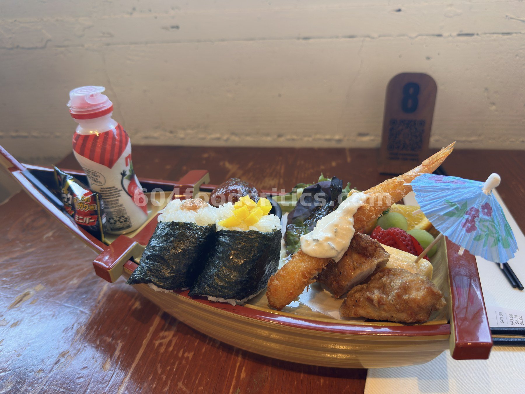 Takenaka Kids Combo served in a wooden boat with two onigiri, ebi fry, karaage, fruit and a paper umbrella