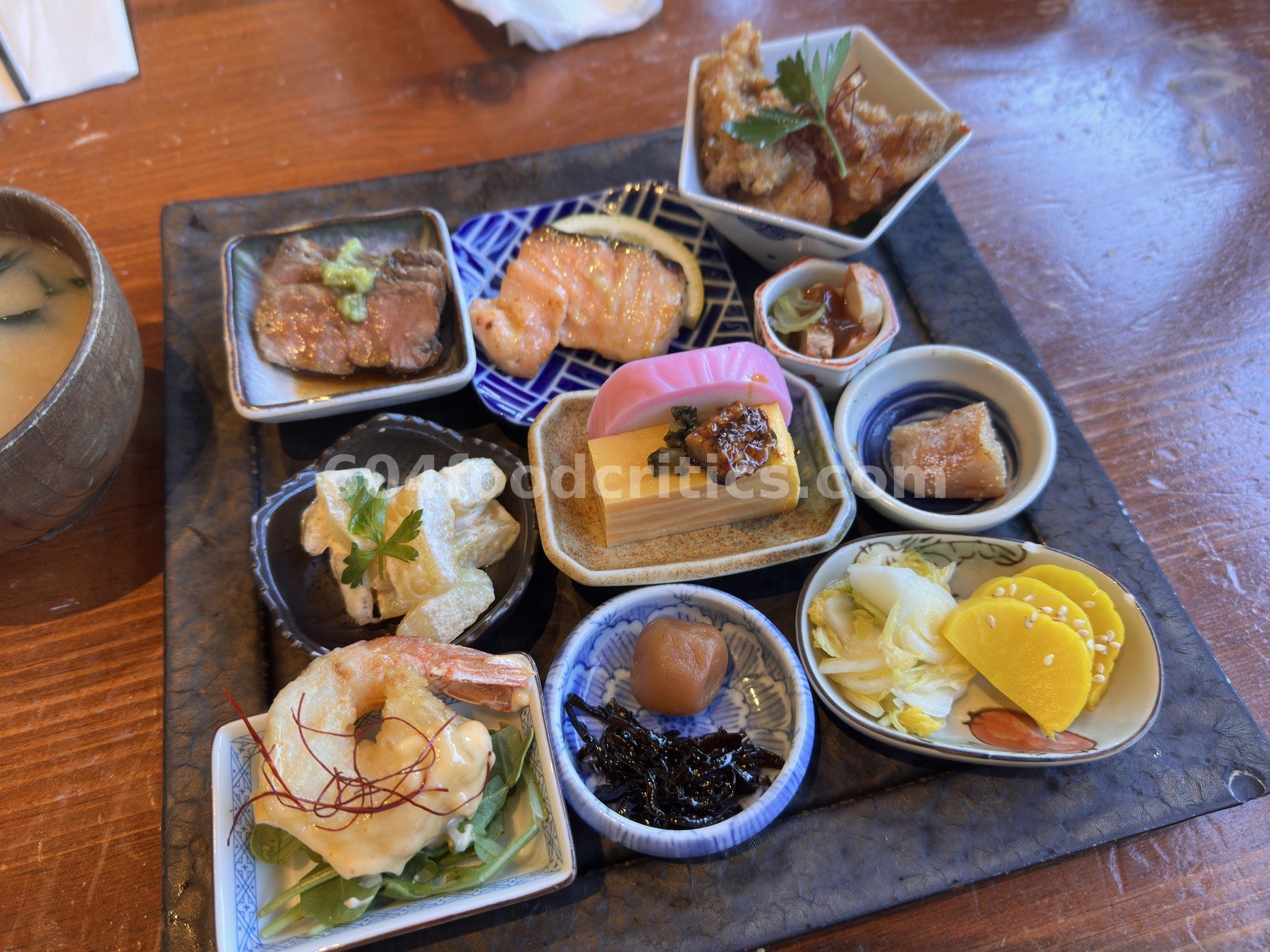 Close view of obanzai small dishes: seared wagyu, grilled salmon, karaage, ebi mayo, tamagoyaki, umeboshi and pickles